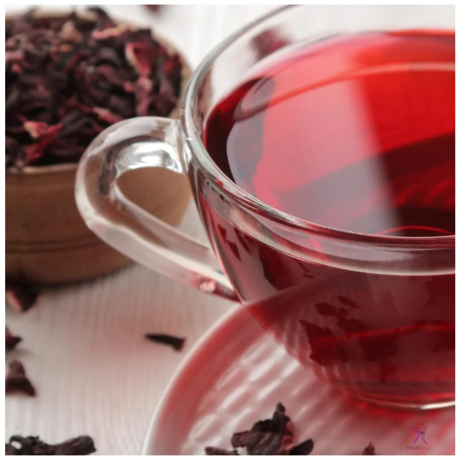 Clear glass mug filled with red zobo tea, surrounded by dried zobo tea leaves.