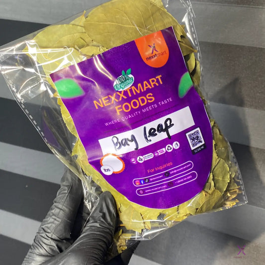 Packaged bay leaves with a Nextmart Foods label held by a gloved hand on a gray surface.